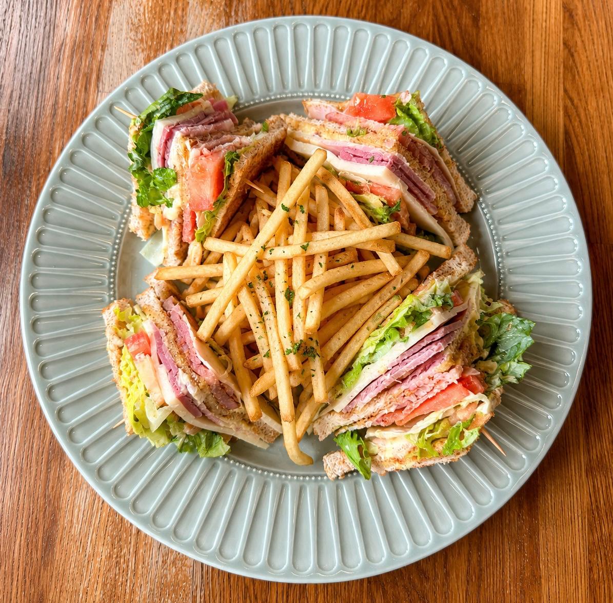 Triple-decker club sandwich with ham, cheese, lettuce and tomato served with fries